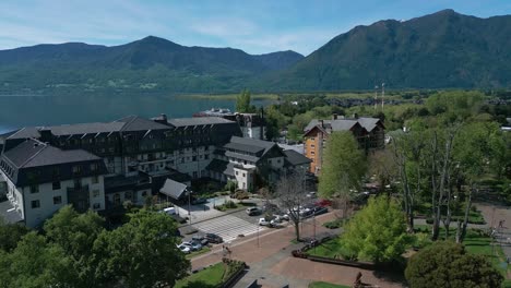 drone shot over the main square of pucón, showing urban park, surrounding buildings, and villarrica lake with mountains in the background