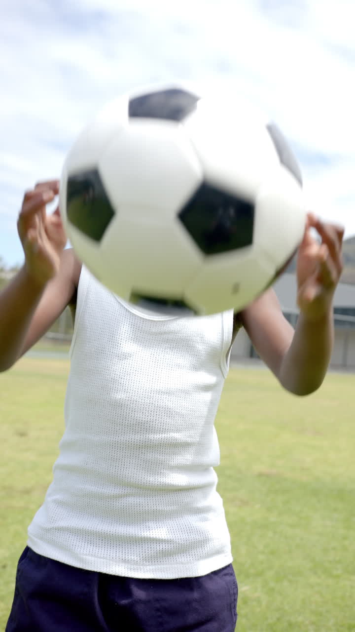 Vertical video: A young African American boy balancing soccer ball on his head