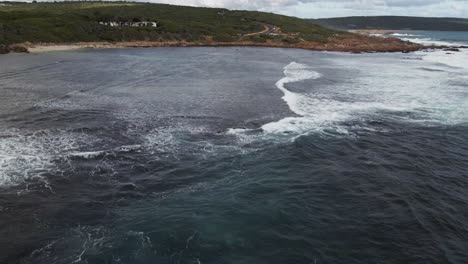 Aerial-flight-over-ocean-with-waves-rolling-and-cars-driving-along-the-coastal-road