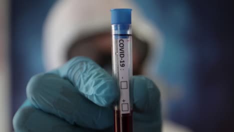 medical researcher's hand with disposable gloves holding a test tube with covid-19 vaccine in the laboratory - close up, rack focus