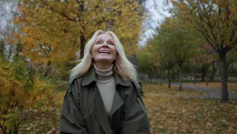 closeup happy elderly lady having fun with foliage in autumn park in slow motion