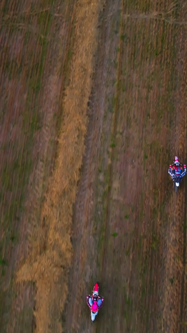 Riding motorbikes in the field with left hay. Happy couple of young people riding their vehicles in the cut farmlands. Bird's eye view. Vertical video