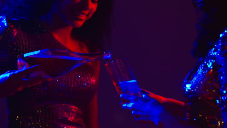 close up of two women in nightclub bar or disco pouring drinks from bottle