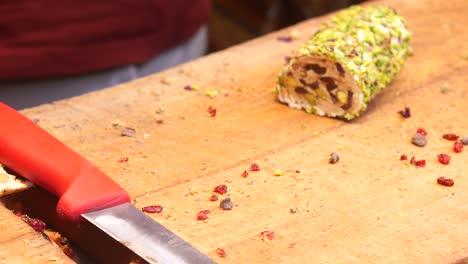 primer plano de una persona cortando delicias turcas cubiertas de pistachos en una tabla de cortar de madera.