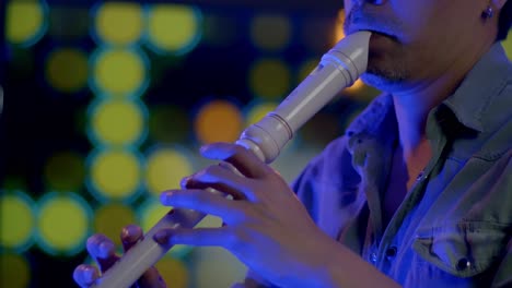 Slow-Motion-Shot-Of-Musician-Playing-Recorder,-Blurry-Colorful-Lights-In-Background