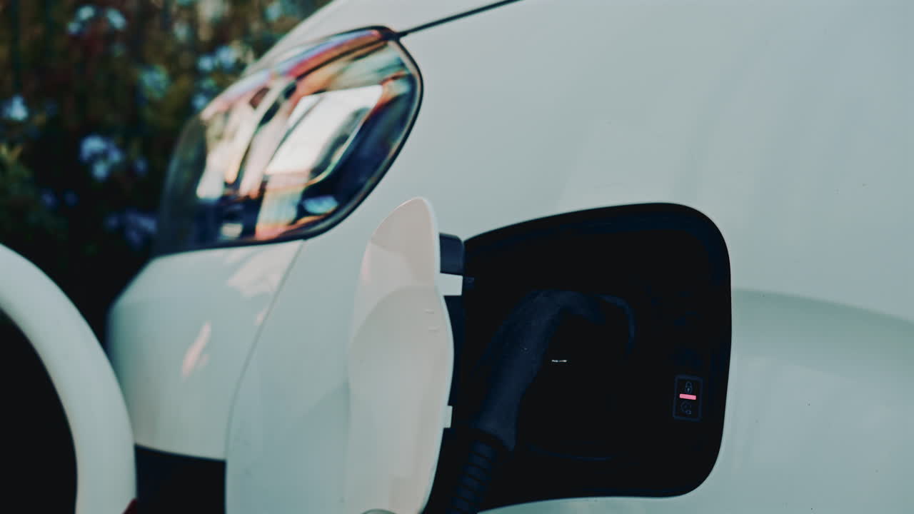 Close up of an electric car being charged, showing the charging port and connector attached to the white vehicle