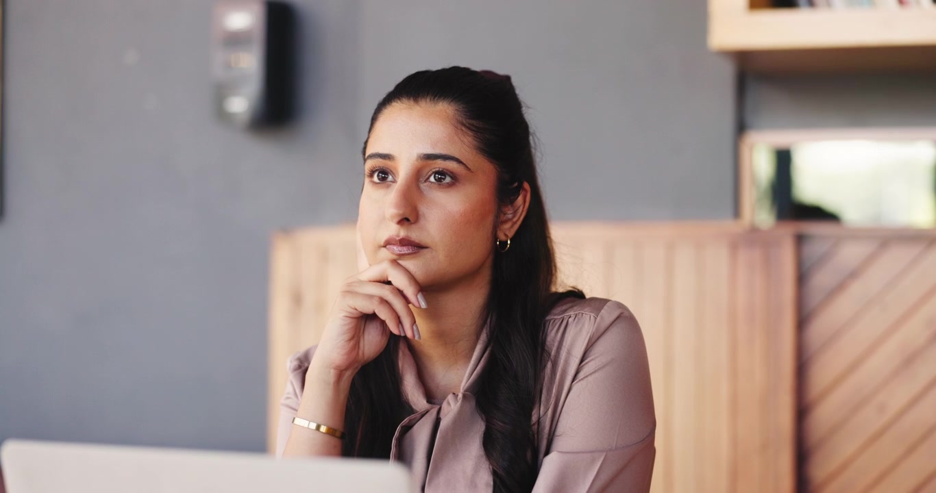 Thoughtful Young Woman Working on Laptop in Office