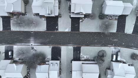 top-down aerial rising view of a snow-dusted street and houses with bare trees