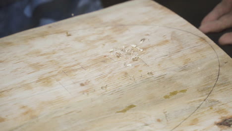 crafstman blowing sawdust from wooden plank with skateboard outline, close up view