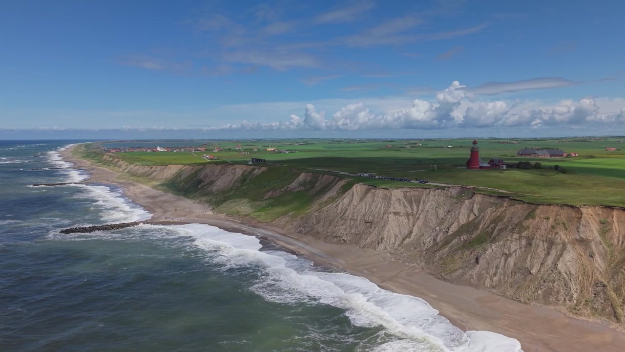 Flygfoto som fångar Bovbjerg fyr längs Nordsjöns kustlinje, omgiven av färgstarka gröna ängar, karga klippor och ett levande kustlandskap på västra Jylland