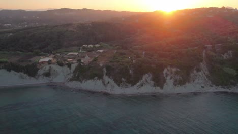 Toma-Aérea-De-Villas-Frente-Al-Mar-En-La-Costa-De-Arillas,-Corfú-Durante-La-Puesta-De-Sol