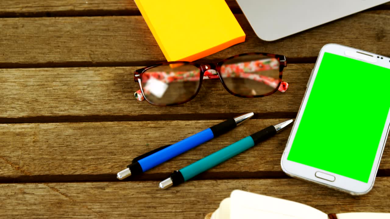 portátil, nota adhesiva, teléfono móvil, bolígrafo, organizador y gafas en la mesa 4k