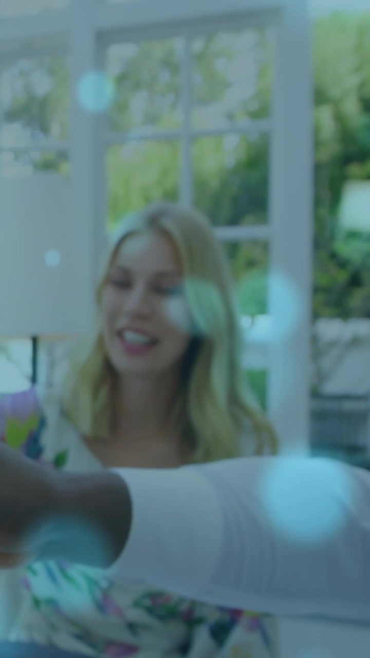 Video verticale: Donna sorridente che si protende al tavolo da pranzo, brindando con il vino, mentre un uomo le porge un oggetto.