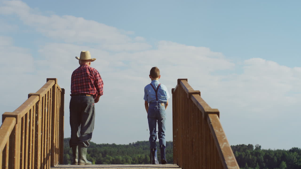 Rear view of a teen boy and his grandfather fishing and throwing their fishing rods to the water in the wooden bridge