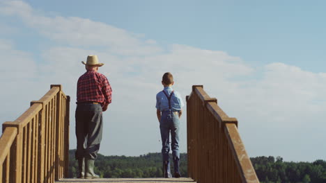 rear view of a teen boy and his grandfather fishing and throwing their fishing rods to the water in the wooden bridge