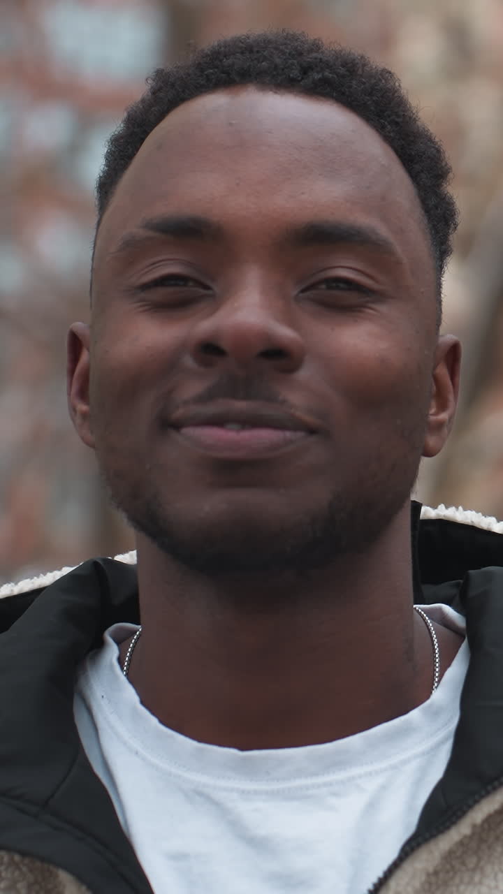 hombre negro elegante se quita la capucha mientras mastica chicle, posando con confianza en un entorno de invierno al aire libre con árboles desnudos en el fondo, encarnando la moda casual y el estilo de vida urbano