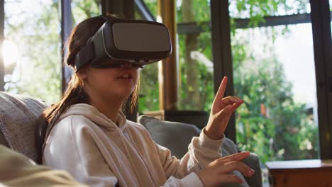 Asiatisches-Mädchen-Lächelt-Und-Gestikuliert,-Während-Es-Ein-VR-Headset-Trägt-Und-Zu-Hause-Auf-Der-Couch-Sitzt