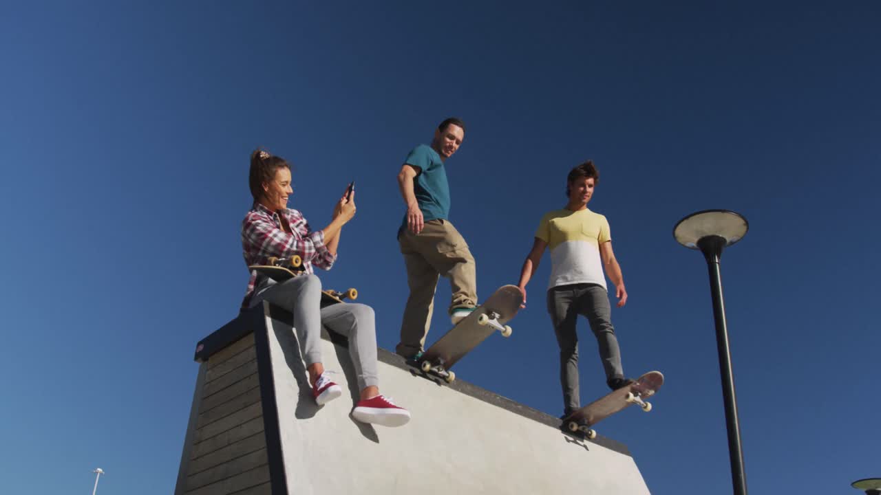 mujer caucásica feliz tomando una foto de sus dos amigos varones patinando