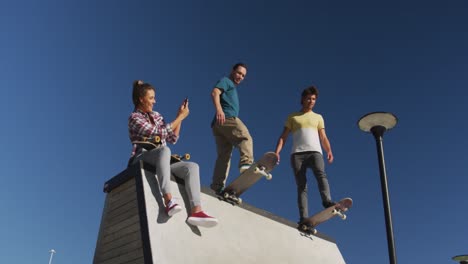 happy caucasian woman taking photo of her two male friends skateboarding