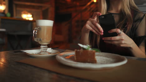 beautiful emotional happy girl is making photo of food in cafe, latte on the table, dessert ice cream chocolate cake cherry mint, communication in social networks