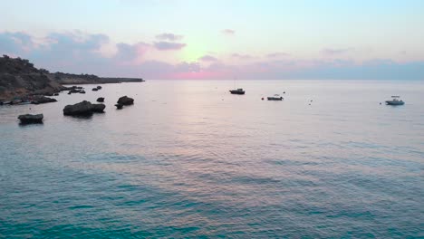 Tiro-Aéreo-Ascendente-Sobre-El-Agua-En-La-Bahía-De-Konnos-Durante-La-Puesta-De-Sol-Con-Brillo-Rosa