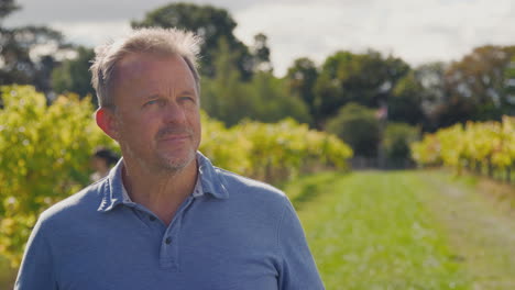 Portrait-Of-Mature-Male-Owner-Of-Vineyard-In-Field-With-Workers-At-Harvest