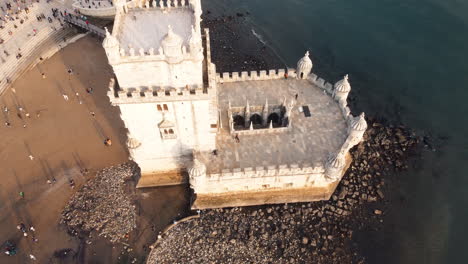 Aerial-tilt-up-shot-of-Torre-de-Belém-with-tourist-and-Atlantic-ocean-in-Lisboa-during-sunset-time,-Portugal