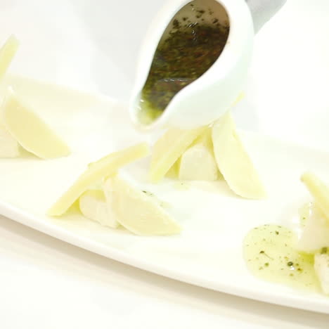 hand with the white cup with green sauce pouring out on the pieces of cheese nicely decorated on a plate. delicious appetizer for guests in the restaurant. close-up