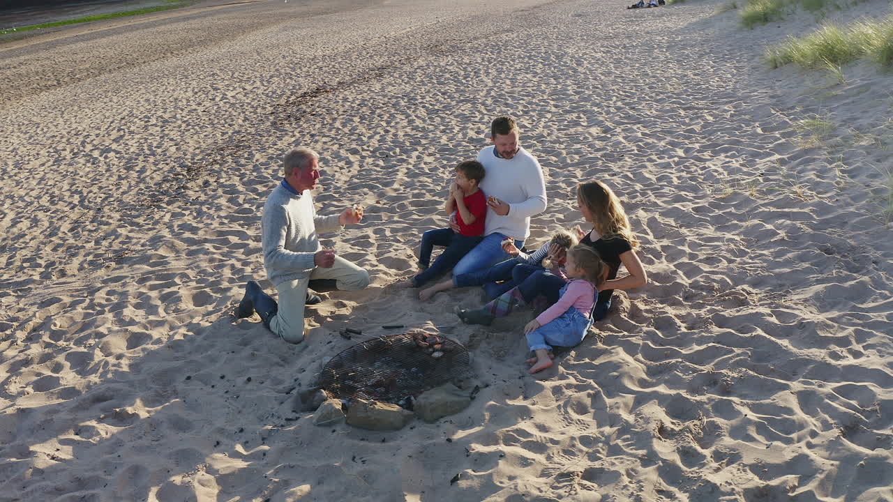 다세대 가족이 해변 휴가에서 불 주위에서 저녁 바베큐를 하는 드론  ⁇