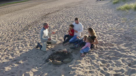 drone shot of multi-generation family having evening barbecue around fire on beach vacation