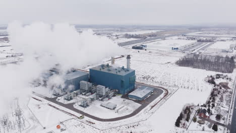 una gran planta industrial que emite vapor en un paisaje nevado, invierno, vista aérea