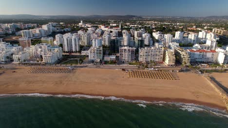 approaching aerial view of beach, boardwalk and buildings in quarteira, algarve, portugal