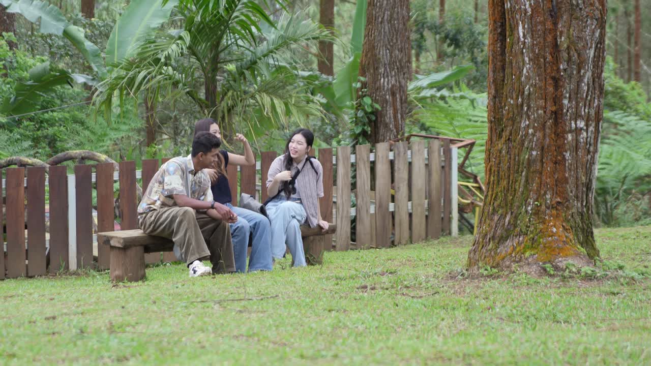 Young Asian Indonesian Friends Sitting Playing Together on a Wooden Bench in Forest Park