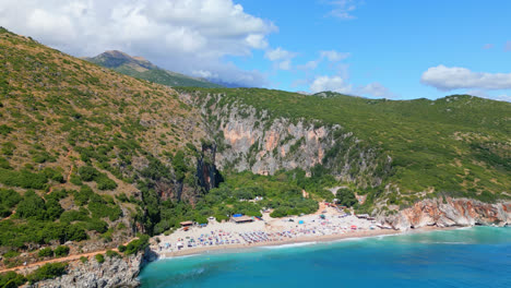 Aerial-drone-forward-moving-shot-over-tourists-sunbathing-along-secluded-Gjipe-beach-in-Albania-on-a-sunny-day