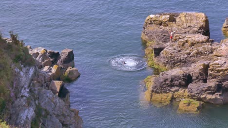 Young-man-in-wetsuit-spins-and-cliff-jumps-into-Irish-Sea,-coastal-town-Howth-Ireland