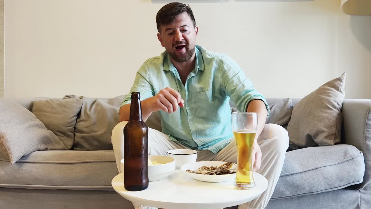 Man relaxing on a couch with beer and dried fish snacks