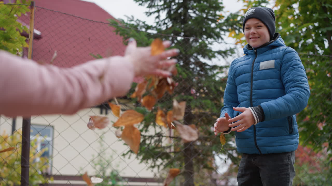 가을의 가족 즐거움: 어린 소년이 놀이를 하면서 잎을 던지고 이모가 더 많이 모으기 위해 구부러지면서, 다채로운 잎자루와 시골 배경에 둘러싸인 기의 순간을 공유합니다.