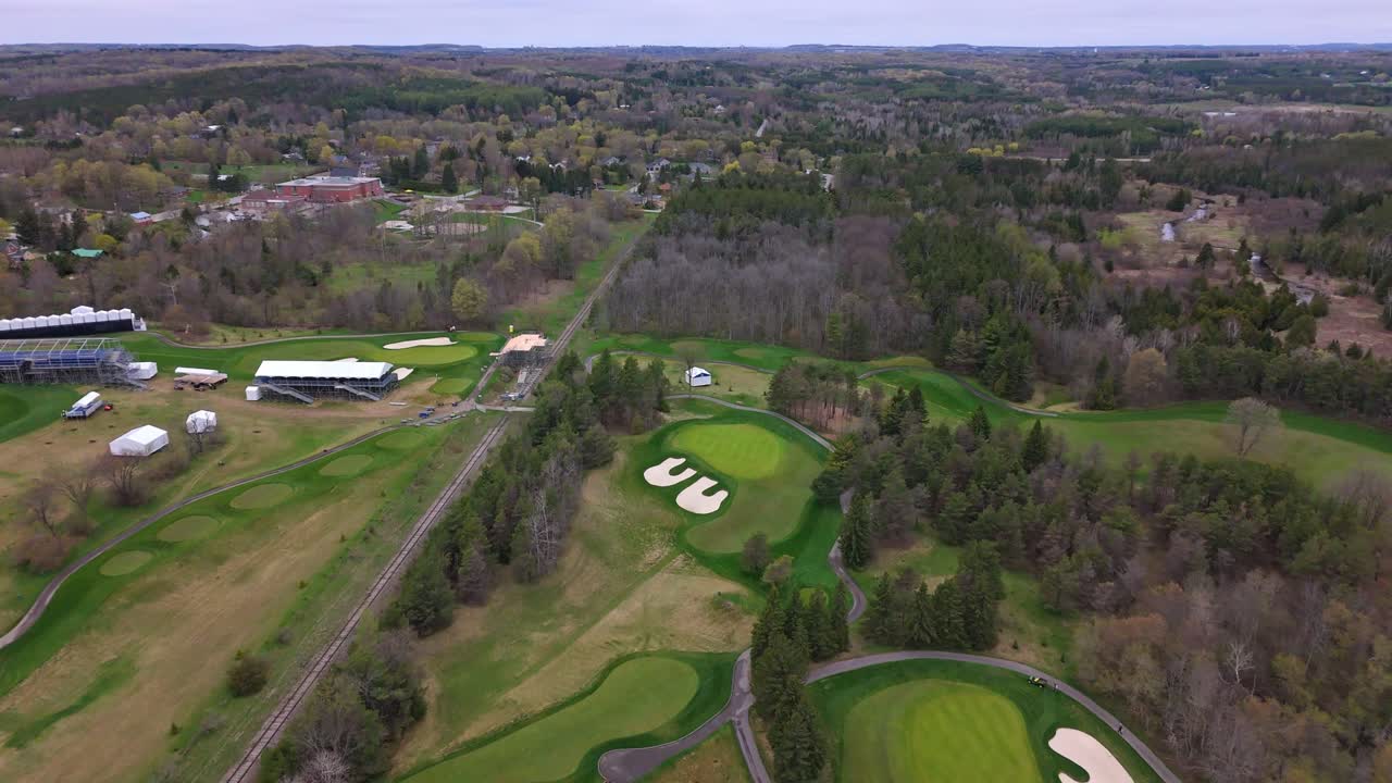 Canadian Golf course between forest trees in Alton, Canada. Aerial forward wide shot. Cloudy day in spring. Neat green grass fields.