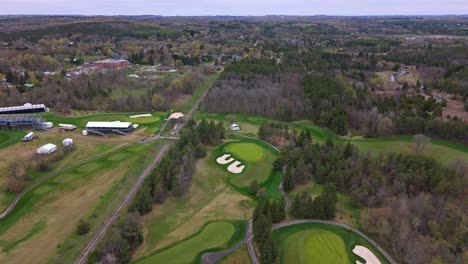 canadian golf course between forest trees in alton, canada. aerial forward wide shot. cloudy day in spring. neat green grass fields.