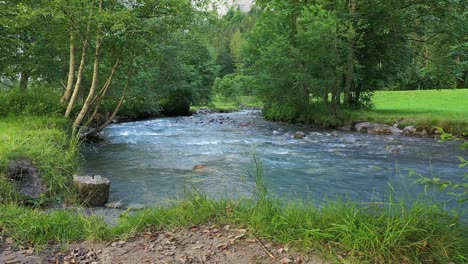 Car-driving-by-on-a-road-beside-scenic-Stream-creek-amid-green-meadows-and-trees-in-Spring