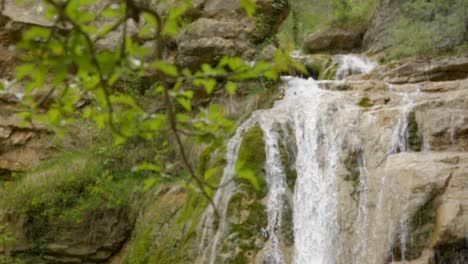 Focus-pull-from-background-waterfall-to-foreground-branches-along-the-Route-of-the-Seven-Pools---Ruta-dels-Set-Gorgs-de-Campdevànol-Catalonia-Spain