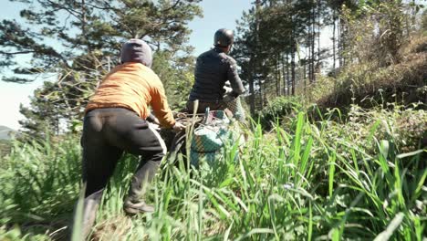 Camera-follow-kid-help-his-father-pushing-motorcycle-on-hillside-path,-Countryside-transportation