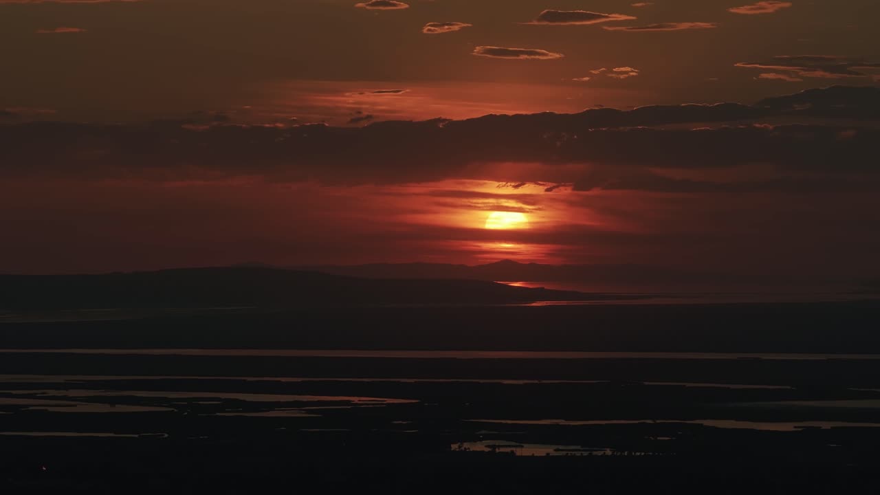 Drone view from Bountiful Canyon in Utah of a golden summer sunset over Salt Lake Valley with clouds, mountains, and water ponds reflecting light from the Great Salt Lake