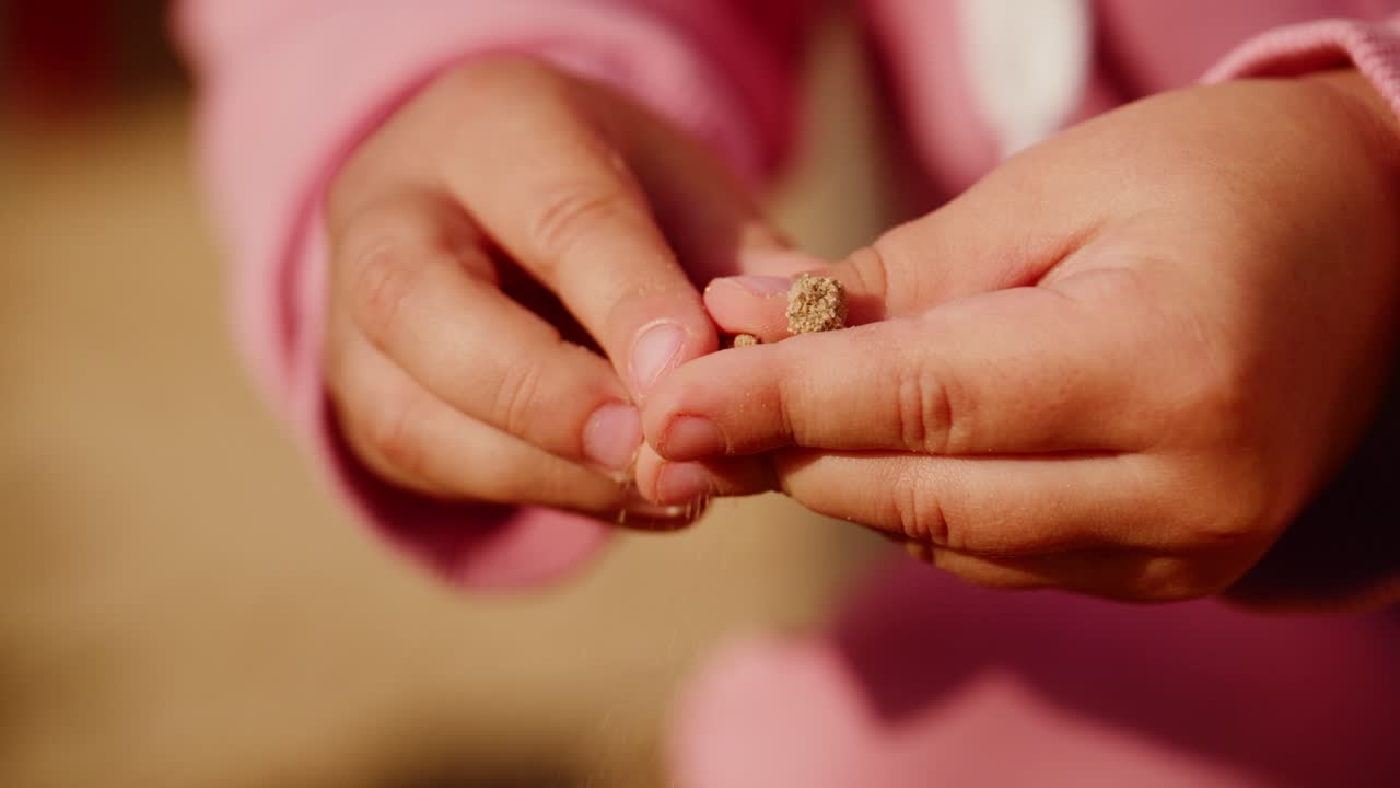 A Child's Hands Gently Holding a Small Object in Pink Apparel, Capturing the Innocence and Curiosity of Youth in a Natural Outdoor Setting