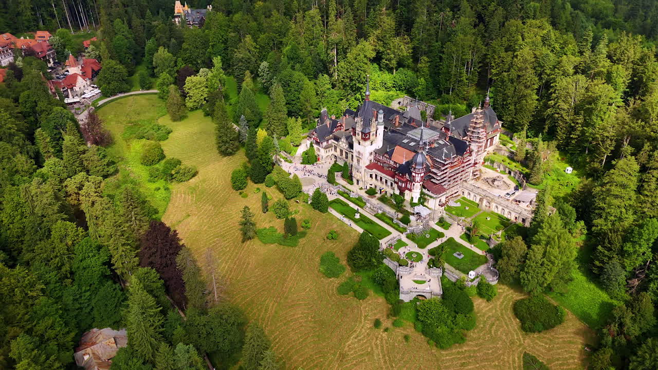 Amazing pine tree woods grow around the stunning Pele? Castle in the Carpathian Mountains, Romania. Drone footage distancing from the famous landmark at daytime