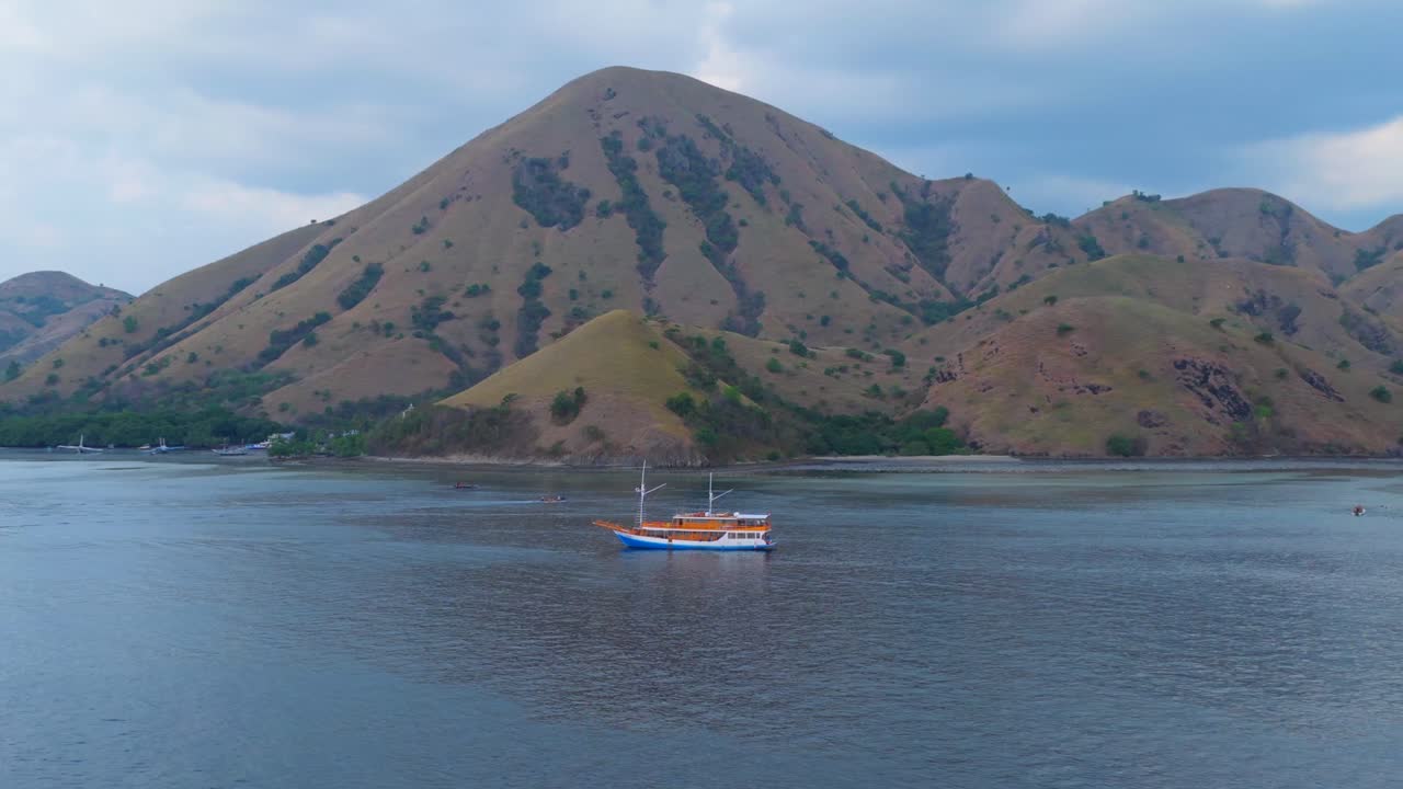 Close-up aerial of a colorful wooden boat anchored near the base of steep golden hills in Komodo National Park
