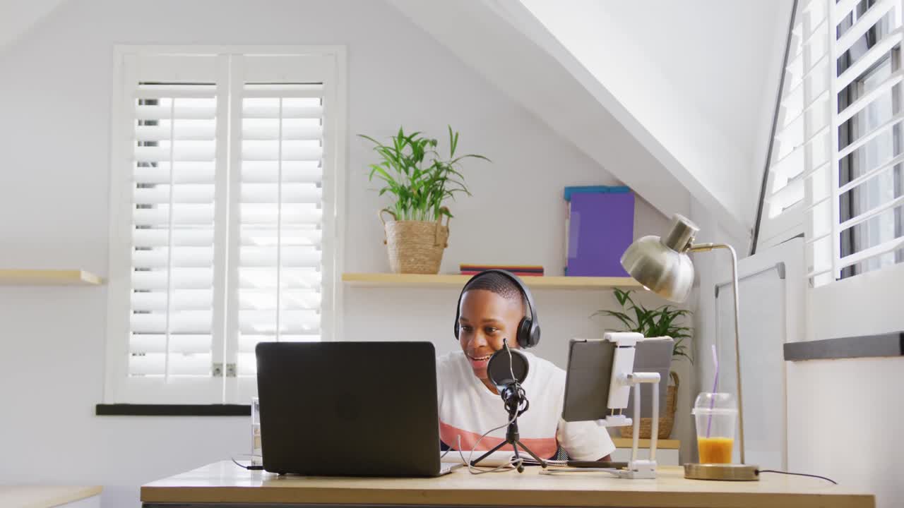 Lykkelig afroamerikansk mannlig tenåring som spiller inn podcast med bærbar PC, sakte film