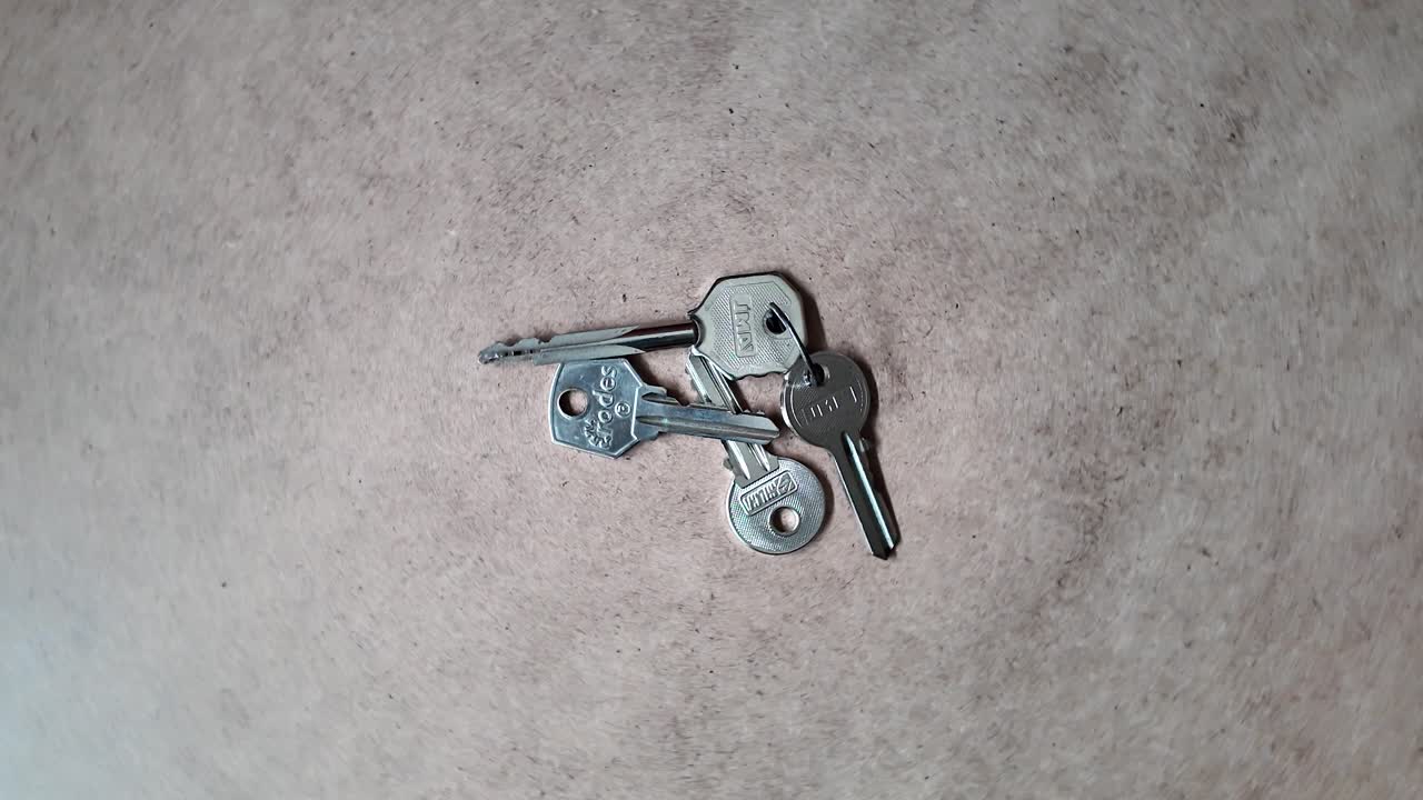 Metal keys rotate on beige textured surface with simple minimalist design
