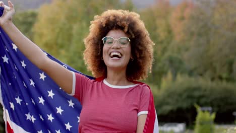 Retrato-De-Una-Mujer-Birracial-Sosteniendo-La-Bandera-De-Estados-Unidos-En-El-Jardín,-Cámara-Lenta