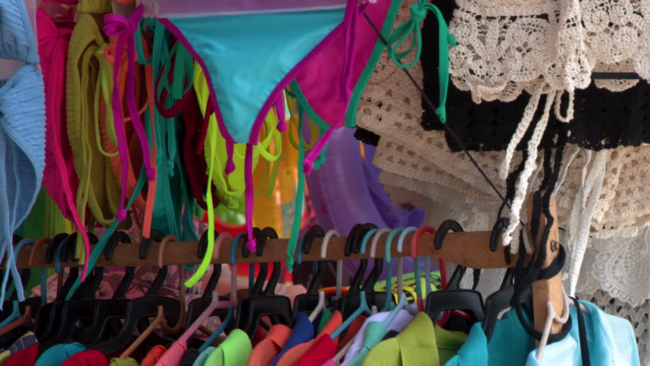 Primo piano di costumi da bagno vivaci e capi in pizzo appesi su stand in un mercato.